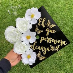 a hand holding a black and white graduation cap with flowers on it that says el que persera alcanga