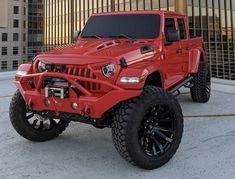 a red jeep parked in front of a tall building with black rims and tires