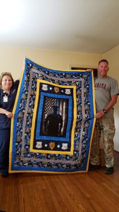 two people standing next to a large quilt