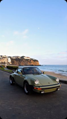 a green car parked on the side of a road next to the ocean in front of a cliff