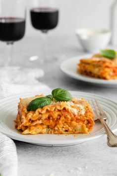 two plates with lasagna and glasses of red wine in the background on a table