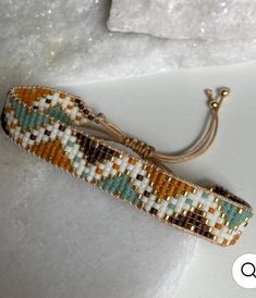 the beaded bracelet is laying on top of some white material and has a gold clasp