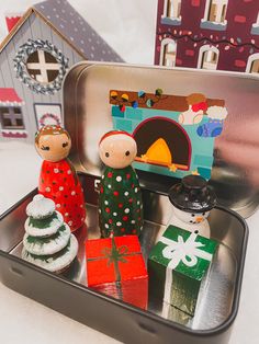 two wooden dolls are sitting in a tin with christmas decorations and gifts on the tray