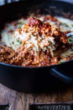 a spoon full of pasta and meat in a skillet on top of a wooden table