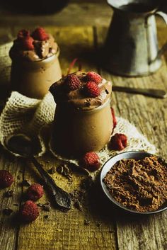 two cups filled with chocolate and raspberries on top of a wooden table next to a spoon