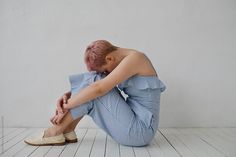 a woman sitting on the floor with her head in her hands, wearing blue and white striped pants