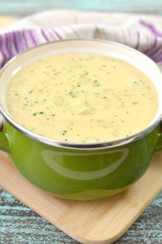 a green bowl filled with soup sitting on top of a wooden cutting board next to a purple and white cloth