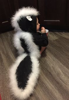 a small child in a black and white costume is holding a cup while sitting on the floor