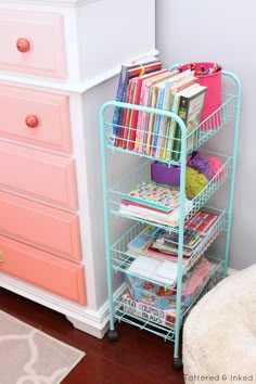 a pink and white dresser with books on it next to a blue metal book rack