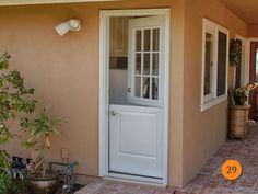 a white door is open on the side of a house with potted plants outside