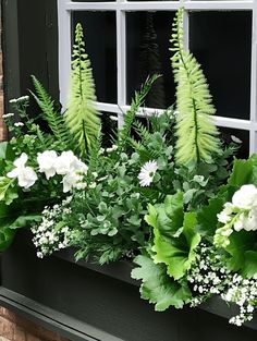 a window sill filled with lots of green plants and white flowers next to a brick building