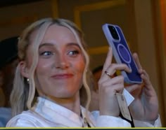 a woman holding up a cell phone in her right hand and smiling at the camera