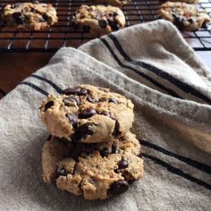 three chocolate chip cookies on a towel next to cooling racks with more cookies in the background