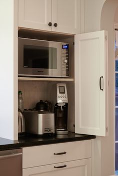 a kitchen with white cabinets and black counter tops, an open microwave oven and coffee maker