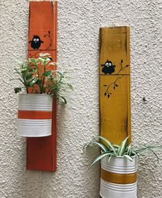 two painted pots with plants in them hanging on the side of a wall next to a planter