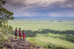 three girls standing on top of a hill looking out at the plains and clouds in the distance