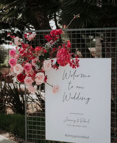 a sign with flowers on it that says welcome to our wedding, in front of a fence