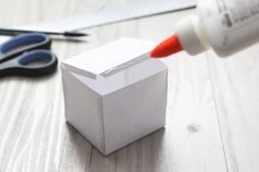 scissors and glue are sitting on the table next to an empty box with a piece of paper sticking out of it