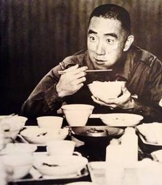 a man sitting at a table eating food with chopsticks in front of him