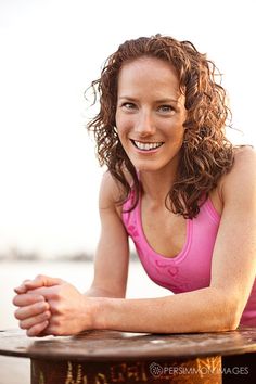 a woman sitting on top of a wooden table next to the ocean with her arms crossed