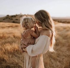 a woman holding a baby in her arms while standing in a field with dry grass