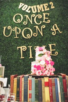 a table topped with books and a cake covered in pink flowers next to a green wall