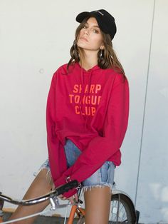 a woman sitting on top of a bike wearing a red hoodie and ripped shorts