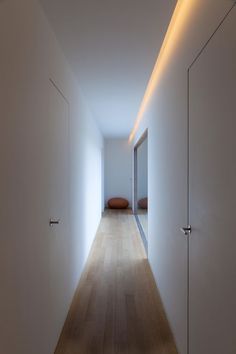 an empty hallway with white walls and wood flooring is lit by recessed lighting