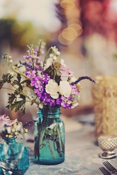 purple and white flowers are in a blue mason jar on a table with silverware