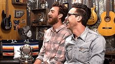 two men sitting next to each other with guitars on the wall in the back ground