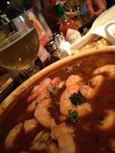 a bowl of soup with shrimp and garnish on the table next to wine glasses