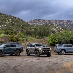 three trucks are parked in a parking lot with mountains in the backgrouds