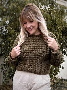 a woman is smiling and holding her hair in one hand while wearing a green knitted sweater