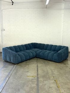 a large blue sectional couch sitting in an empty room with white walls and concrete flooring