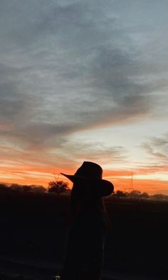 a person wearing a cowboy hat standing in front of a sky with the sun setting