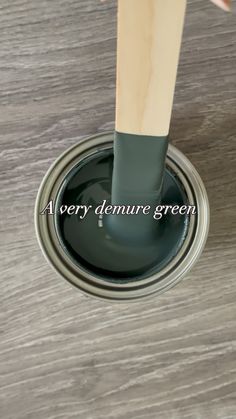 a person is holding a paintbrush over the top of a gray painted can with text that reads, a very demure green