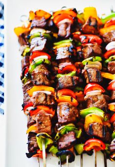 skewered meat and vegetables on a white platter with red, green, yellow and orange peppers