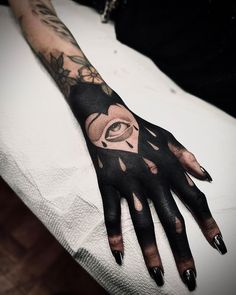 a woman's hand with black and white tattoos on her left arm, which has an eye in the middle