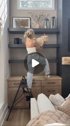 a woman is standing on a ladder in her living room and she is holding a stuffed animal