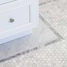 a white bathroom with hexagonal tiles on the floor and vanity in the corner