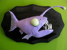 a purple fish with an egg in it's mouth sitting on a black plate