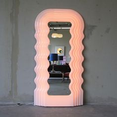 a large pink mirror sitting on top of a floor next to a table with a lamp