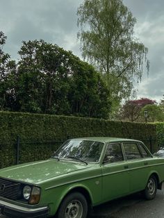 an old green car parked in front of a hedge