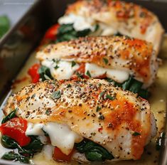 two pieces of chicken covered in cheese and spinach on a baking pan with sauce