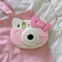 a pink and white hello kitty camera laying on top of a bed next to a pillow