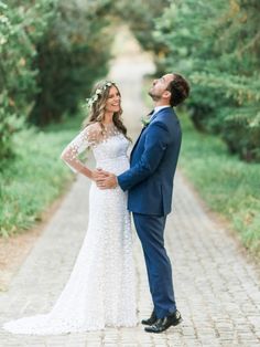 a bride and groom are standing on a brick path in the middle of some trees