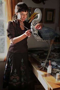 a woman is painting a large bird on a table