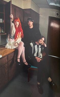 three people sitting on a counter in a kitchen