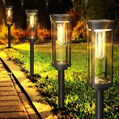 three solar powered lights on the side of a sidewalk in front of grass and trees