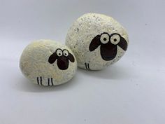 two painted rocks with black and white sheep faces on them, sitting next to each other